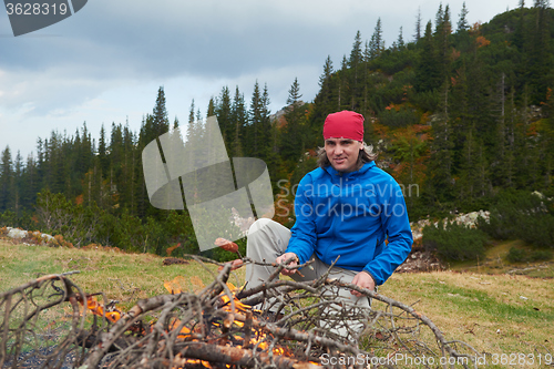 Image of hiking man prepare tasty sausages on campfire