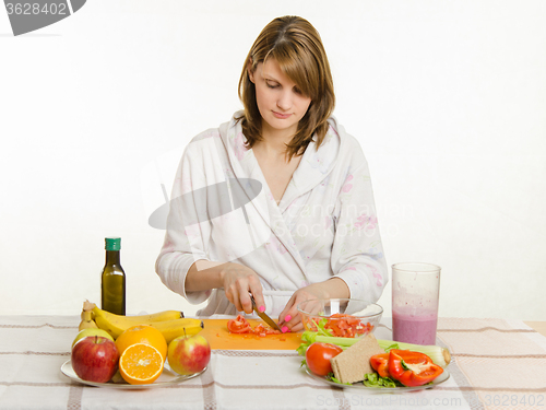 Image of Happy housewife sitting at the table and cut the tomato salad