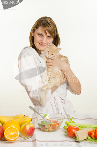 Image of Young girl sitting at the table with vegetarian dishes and holds a disgruntled cat