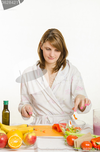 Image of Housewife throws sliced peppers in a bowl of salad
