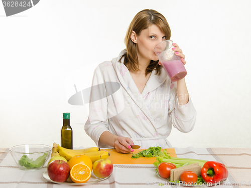 Image of Young girl sitting at the kitchen table, drinking a fruit milkshake from a large cup