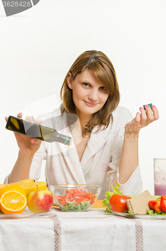 Image of Young woman pouring oil into a vegetarian vegetable salad