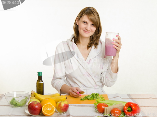 Image of Young girl sitting at the kitchen table and holds a big glass of cocktail