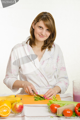 Image of Housewife sitting at the table and cuts the greens for salad