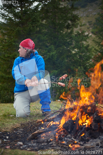 Image of hiking man prepare tasty sausages on campfire