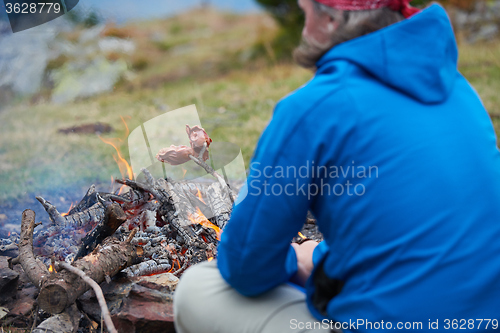 Image of hiking man prepare tasty sausages on campfire