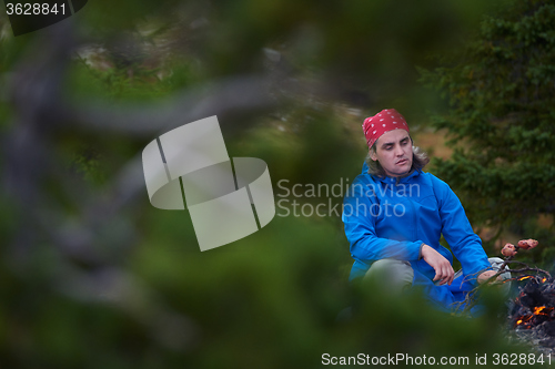 Image of hiking man prepare tasty sausages on campfire