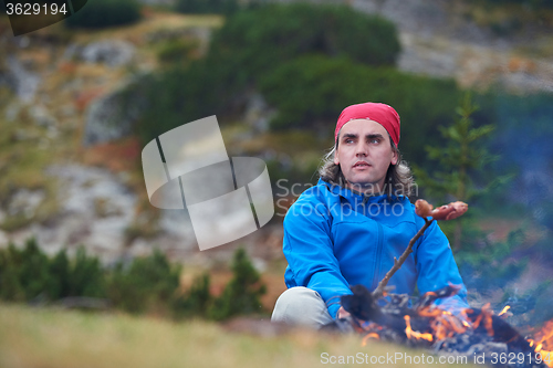 Image of hiking man prepare tasty sausages on campfire