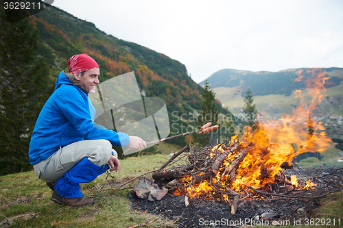 Image of hiking man prepare tasty sausages on campfire