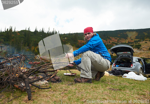 Image of hiking man prepare tasty sausages on campfire