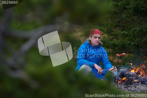 Image of hiking man prepare tasty sausages on campfire