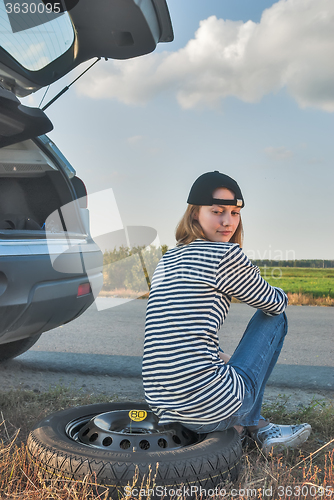 Image of Young sad woman sits on spare wheel