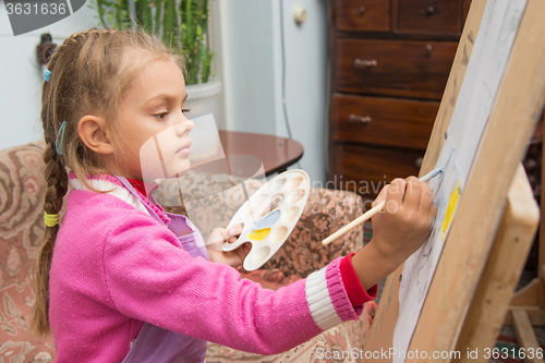 Image of The girl draws a picture paints on an easel in the studio of the artist