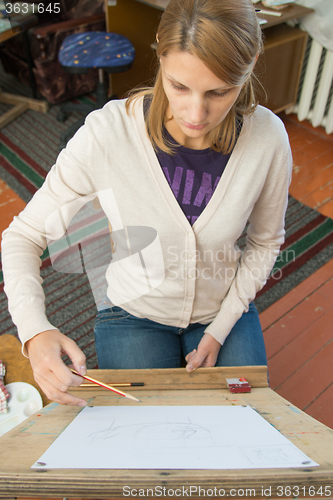 Image of A young girl paints on an easel in the studio of the artist