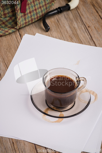 Image of Coffee cup, paper sheets and detective hat