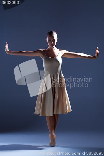 Image of Young beautiful dancer in beige dress dancing on gray background