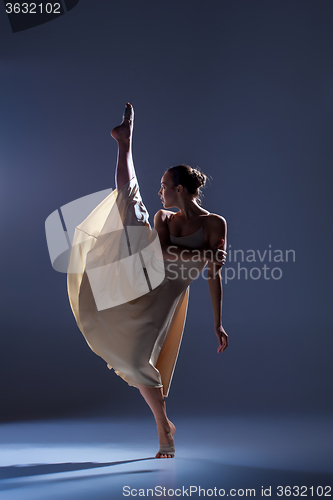 Image of Young beautiful dancer in beige dress dancing on gray background