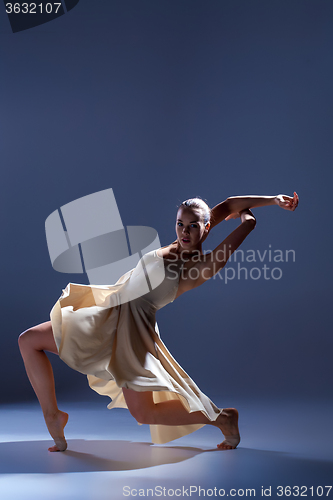 Image of Young beautiful dancer in beige dress dancing on gray background