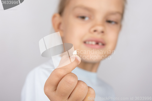Image of Six year old girl holding a fallen tooth and smiling looking at him