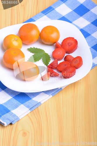 Image of A slice of red strawberry on white plate with mandarin and strawberry slices