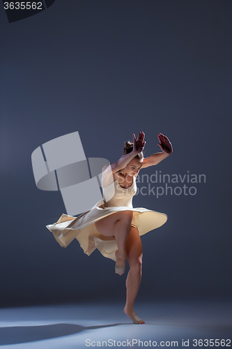 Image of Young beautiful dancer in beige dress dancing on gray background