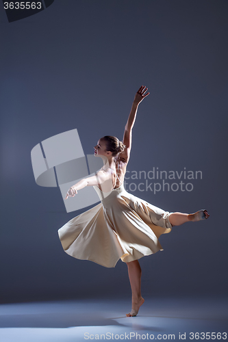 Image of Young beautiful dancer in beige dress dancing on gray background