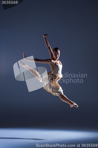Image of Young beautiful dancer in beige dress jumping on gray background