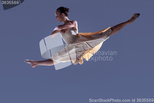 Image of Young beautiful dancer in beige dress jumping on gray background