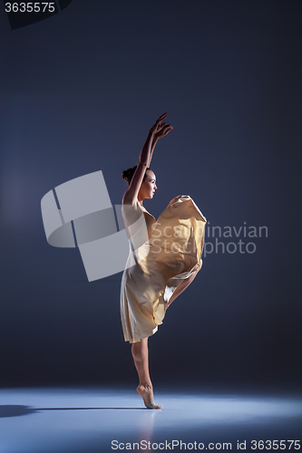 Image of Young beautiful dancer in beige dress dancing on gray background
