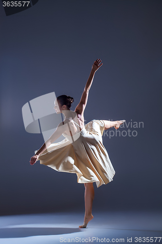 Image of Young beautiful dancer in beige dress dancing on gray background