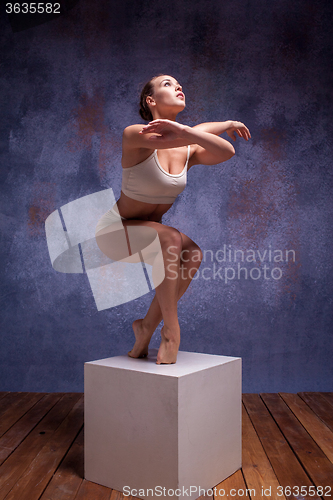 Image of Young beautiful dancer in beige swimwear posing on white cube
