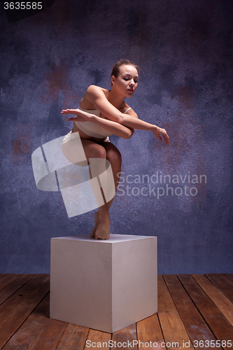 Image of Young beautiful dancer in beige swimwear posing on white cube