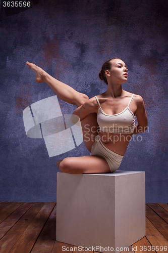 Image of Young beautiful dancer in beige swimwear posing on white cube