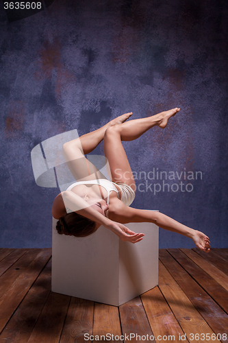 Image of Young beautiful dancer in beige swimwear posing on white cube