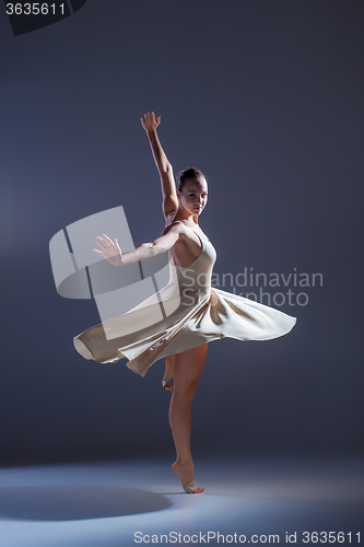 Image of Young beautiful dancer in beige dress dancing on gray background