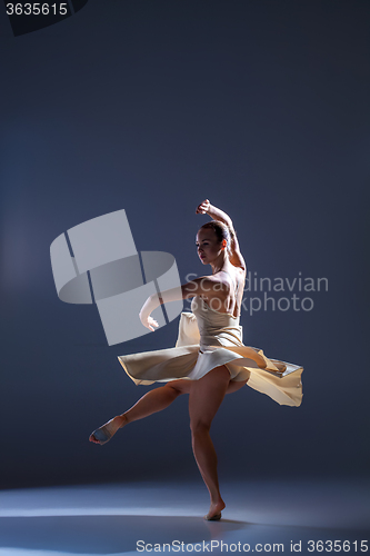 Image of Young beautiful dancer in beige dress dancing on gray background