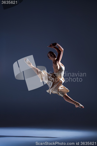Image of Young beautiful dancer in beige dress jumping on gray background