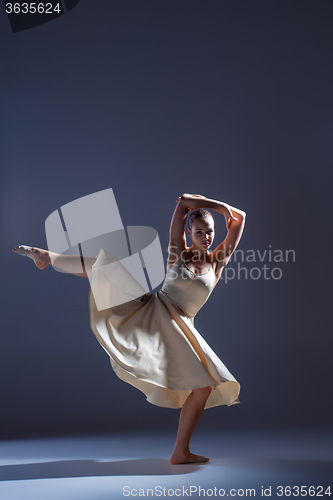 Image of Young beautiful dancer in beige dress dancing on gray background