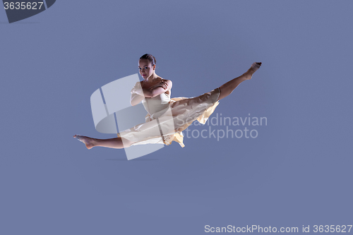 Image of Young beautiful dancer in beige dress jumping on gray background