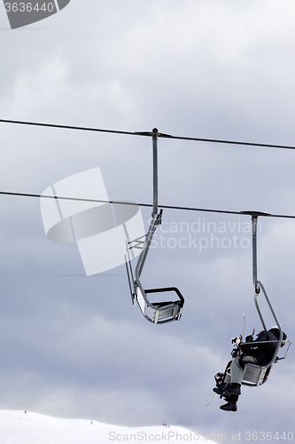 Image of Snowboarders in chair lift at gray windy day