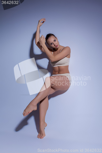 Image of Young beautiful dancer in beige swimwear dancing on lilac background