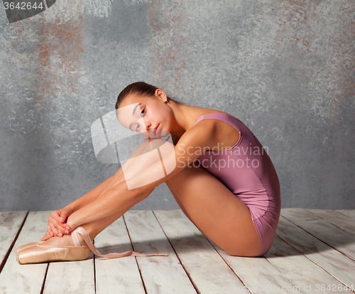 Image of The young ballerina sitting on the wooden floor 