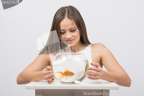 Image of Pretty girl examines a goldfish in an aquarium