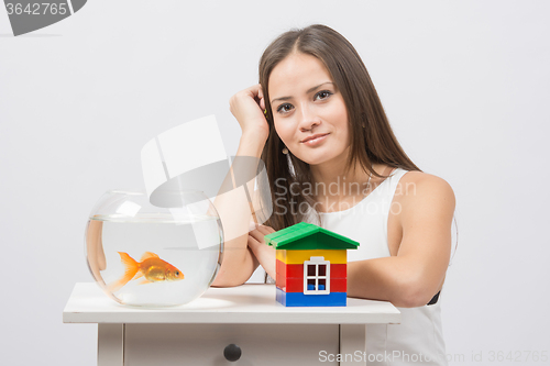 Image of The girl sits at a table on which there is an aquarium with goldfish and toy house