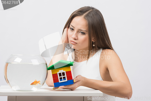 Image of She knocks on the wall of the house a toy aquarium with goldfish