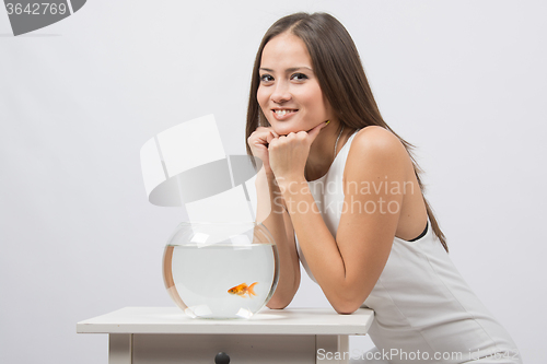 Image of The girl sits near the aquarium with goldfish and looks in the picture