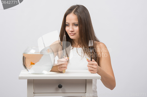 Image of Girl holding knife and fork in hand and with an appetite for looking at the little goldfish