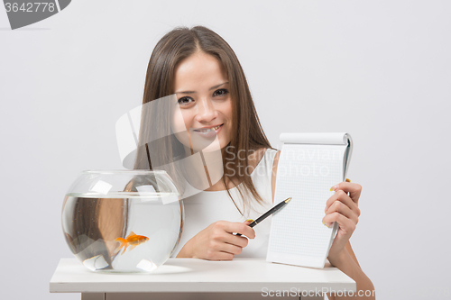 Image of Girl shows a pen entry pad, standing next to an aquarium with goldfish