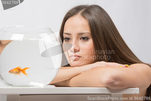 Image of Sad young girl looks at a small goldfish