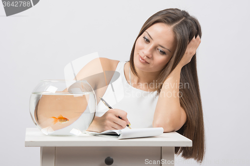 Image of Girl writing in a notebook desire to fulfill a goldfish